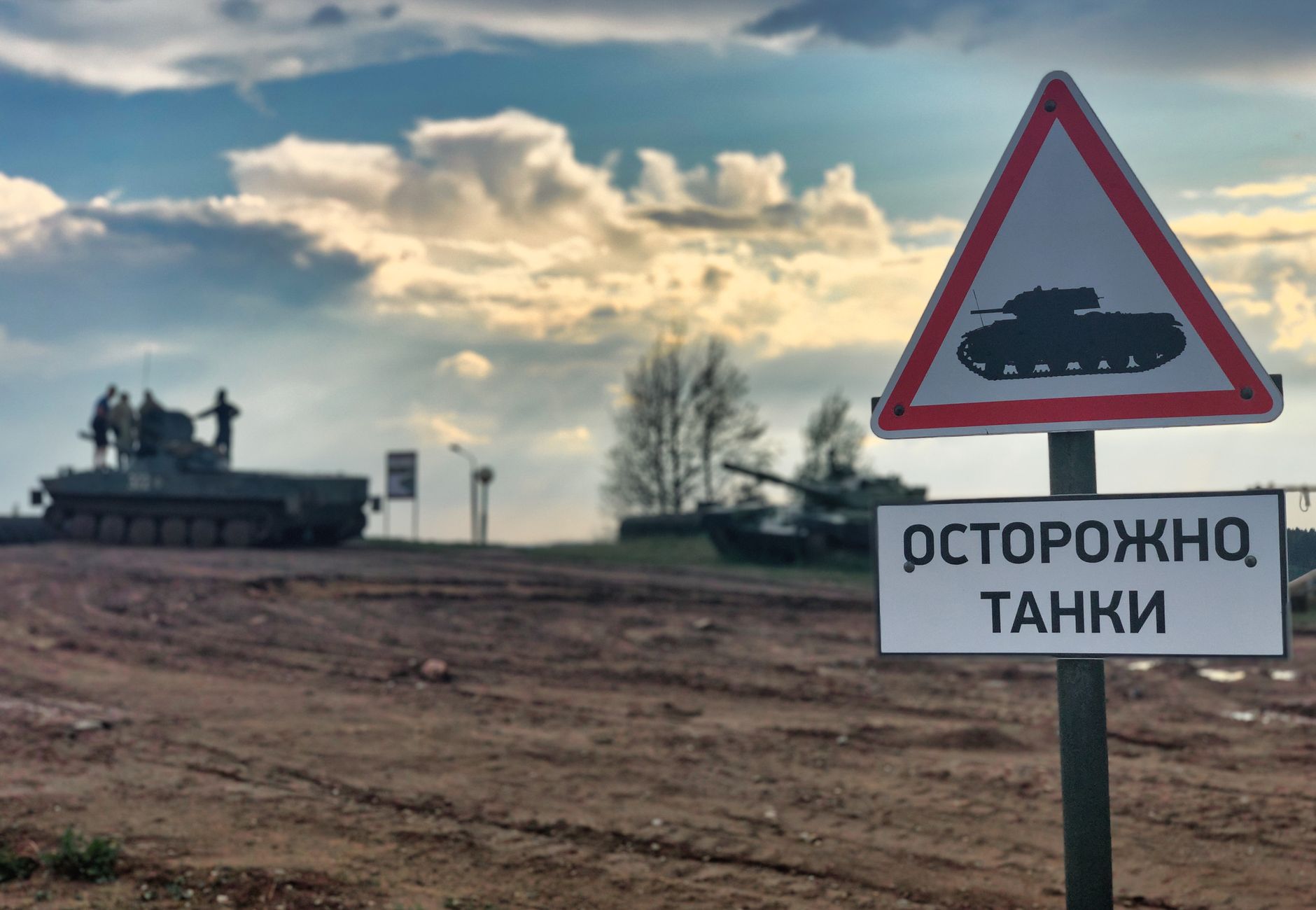 Military tanks in Belarus with a warning sign for caution on dirt road.