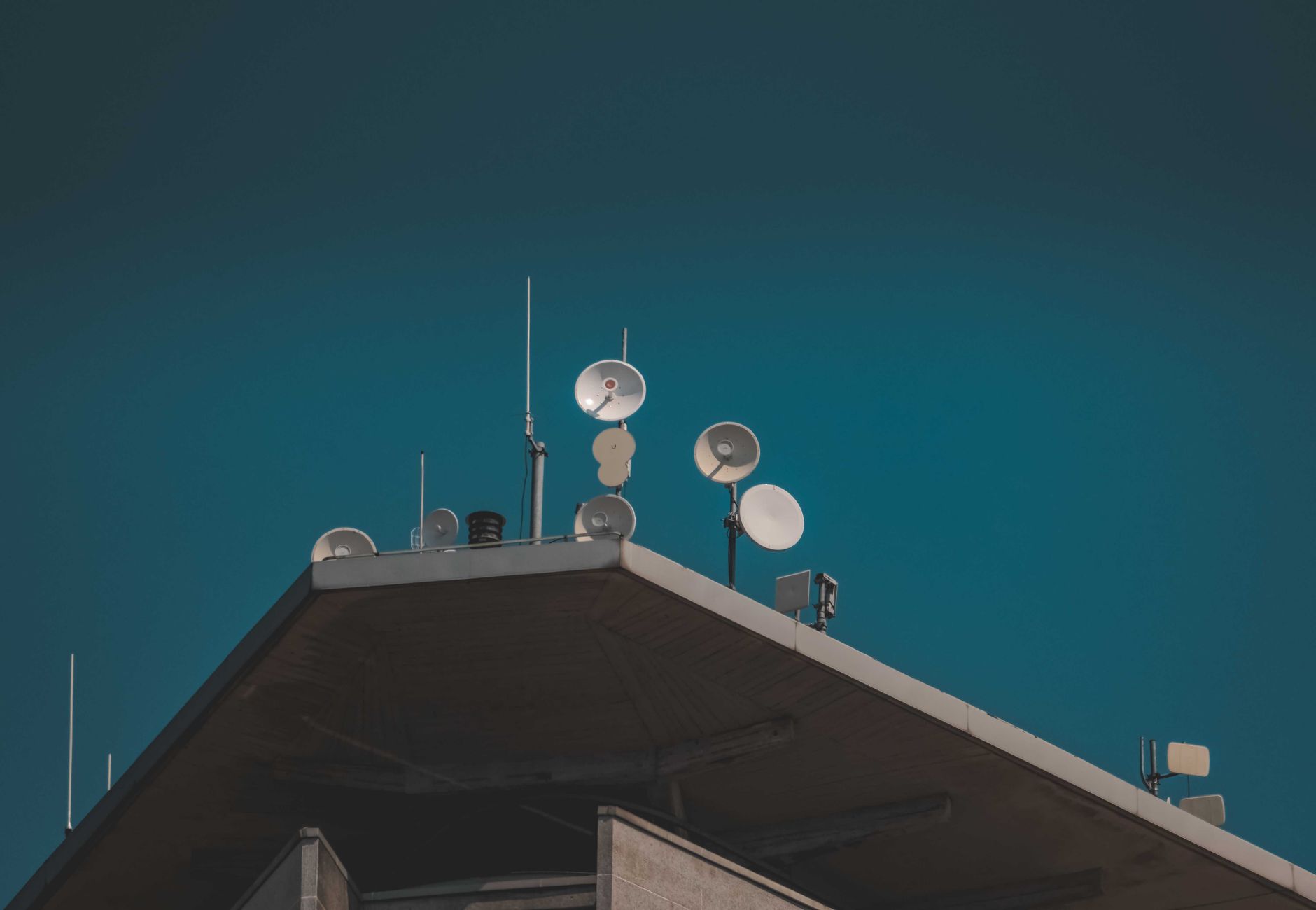 A low-angle view of communication dishes and antennas on a building against a clear blue sky.