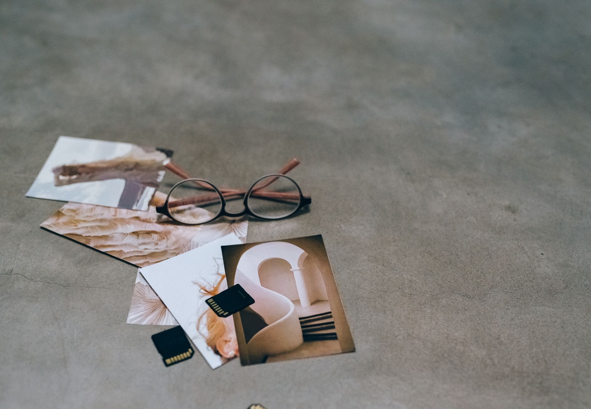 A creative flat lay of eyeglasses, printed photos, and memory cards on a concrete surface.